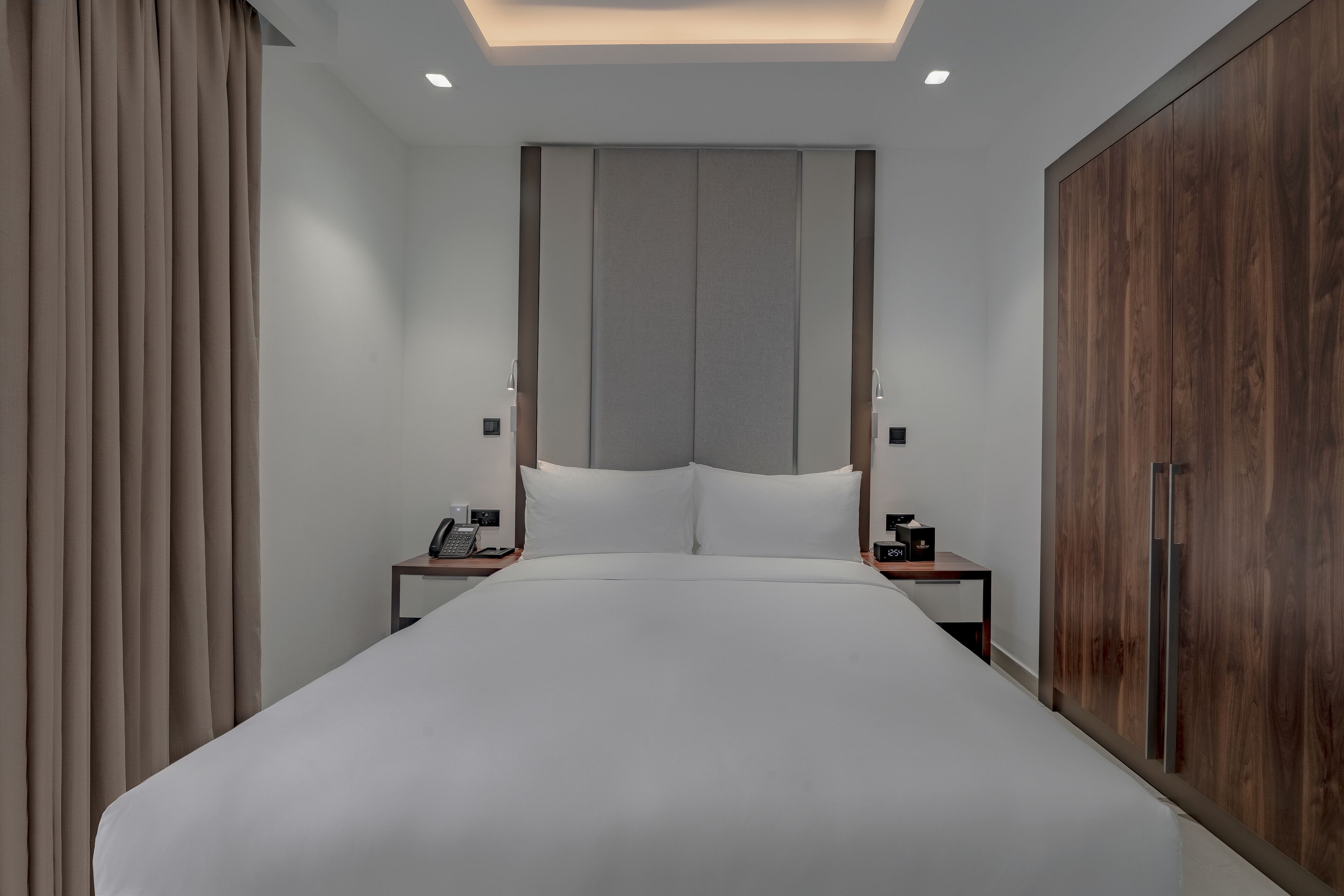A modern hotel room with a large bed, bedside tables, a wardrobe, and a ceiling light.