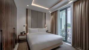 Una habitación de hotel moderna con una cama grande, una mesita de noche, una lámpara y una puerta corrediza de vidrio al balcón.