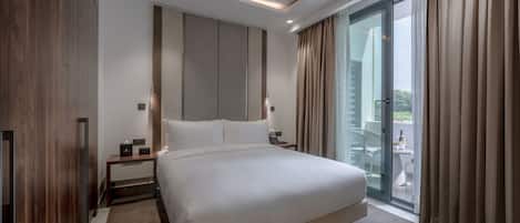 Una habitación de hotel moderna con una cama grande, una mesita de noche, una lámpara y una puerta corrediza de vidrio al balcón.
