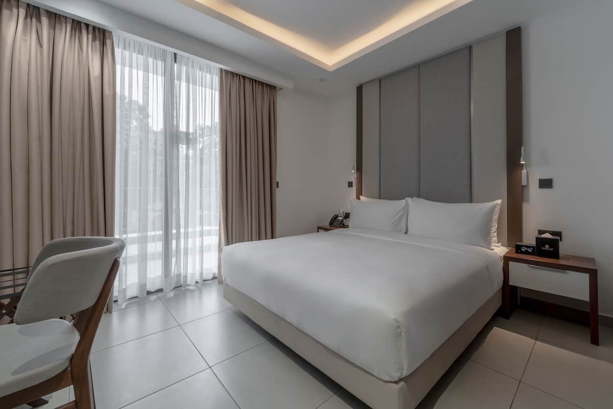 A modern hotel room with a large bed, a bedside table with a clock, and a chair.