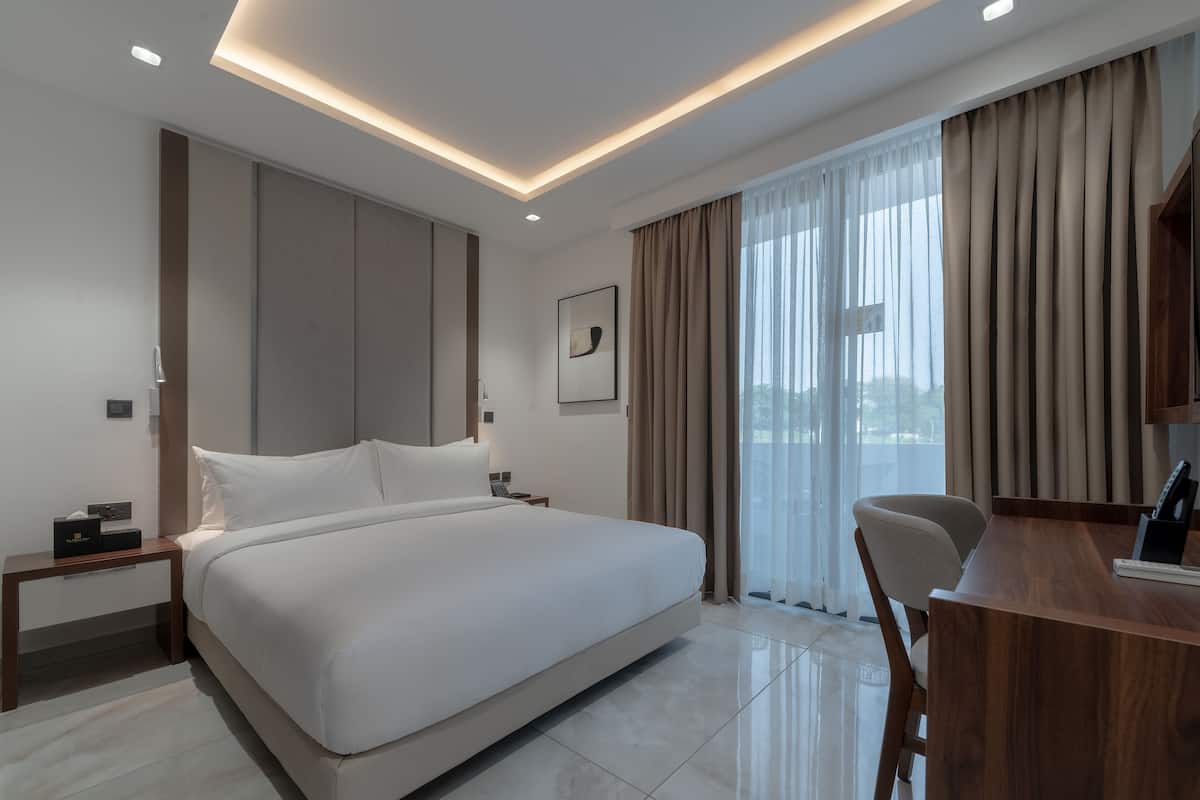 A modern hotel room with a large bed, a desk, and a view of the city.