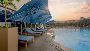 Zona junto a la piscina con sillas de descanso y sombrillas, piscina y valla.