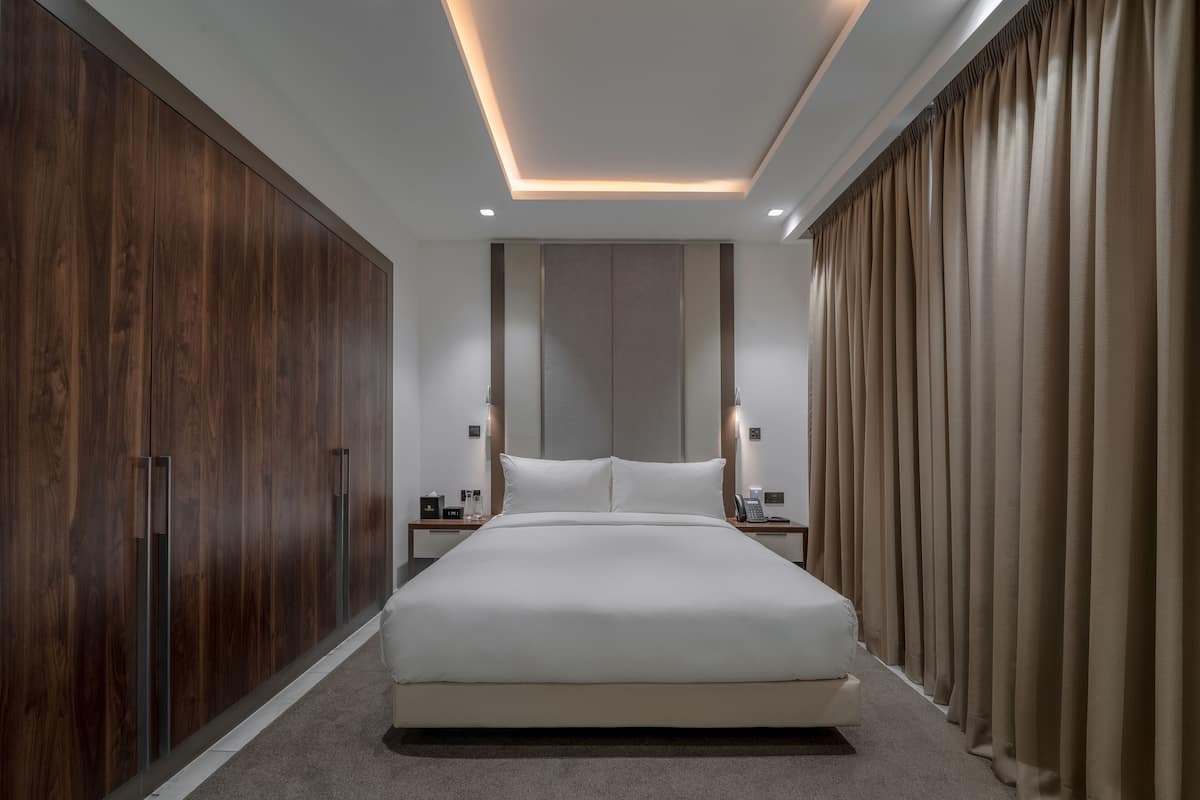 A modern bedroom with a large bed, wooden wardrobe, and a neutral color scheme.