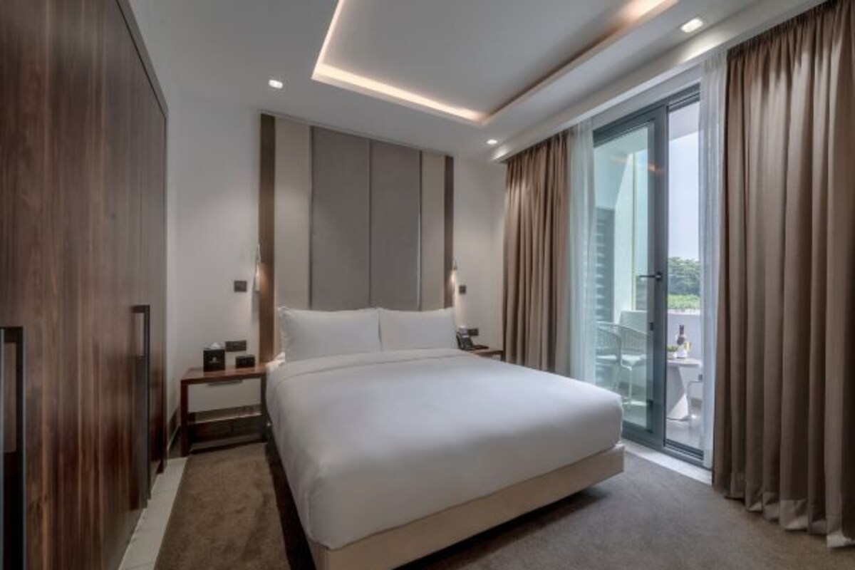 Ein modernes Hotelzimmer mit einem großen Bett, einem Nachttisch, einem Schreibtisch und einer Schiebetür zum Balkon.