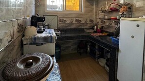 A compact kitchen with a marble backsplash, a window with yellow curtains, a hanging light fixture, and a white refrigerator. - Cozy 2-bedroom apartment in enjoyable Agadir with WiFi (Agadir)