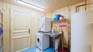 Ett tvättrum med träväggar, en tvättmaskin, en torktumlare, ett handfat och en röd hink.