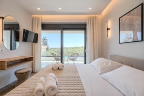 A modern hotel room with a large bed, a flat-screen TV, a balcony with chairs, and a view of the outdoors.