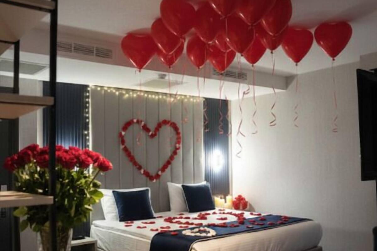 A bedroom with a bed, heart-shaped decorations, red balloons, and a vase of flowers.
