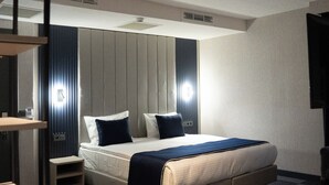 Ein modernes Hotelzimmer mit einem großen Bett, Nachttischen, einem Schreibtisch und einem Flachbildfernseher.