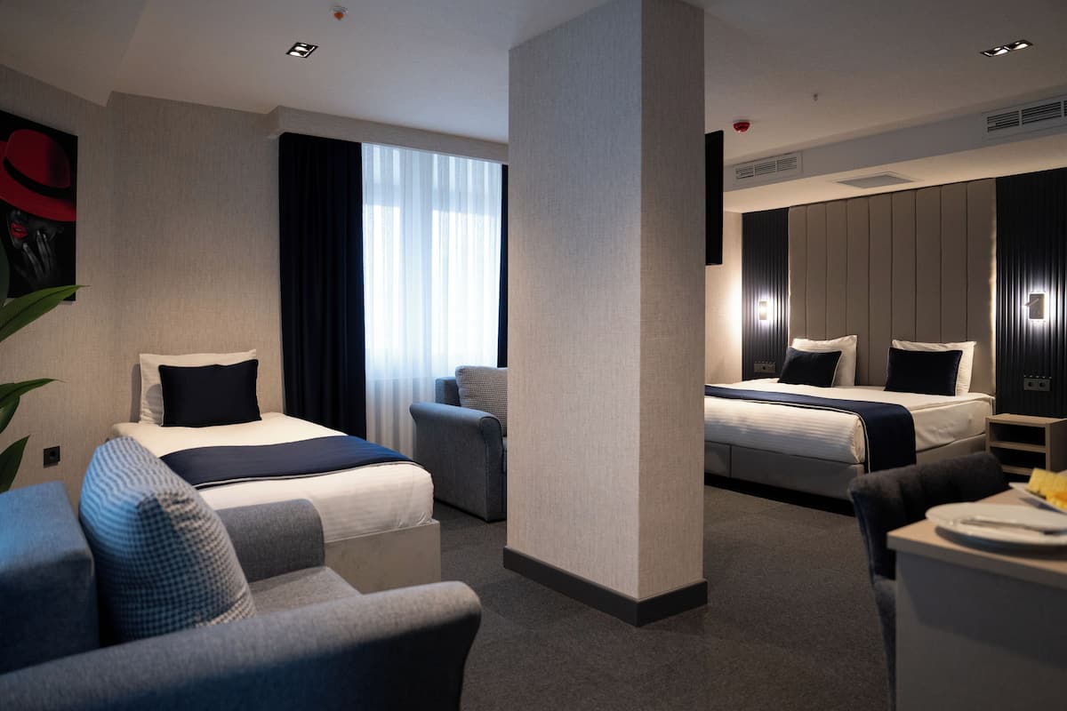 A hotel room with two beds, a sofa, a desk, and a large window with curtains.