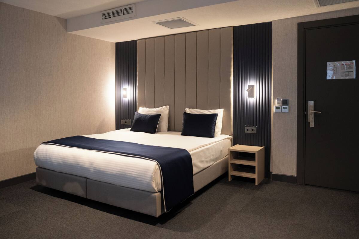 A modern hotel room with a large bed, bedside tables, a wardrobe, and a wall-mounted light fixture.