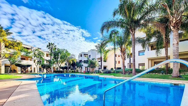 Ein Swimmingpool mit klarem, blauem Wasser, umgeben von Palmen und modernen Gebäuden.