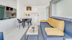 A modern living room with a blue sofa, a coffee table, and a dining area with a table and chairs. - Bal One bedroom apartment Adults Only (203) (Arona)