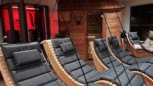Ein Wellnessbereich mit mehreren Holzliegen und blauen Kissen, einem Massagesessel mit roter Beleuchtung und einer Holzwand mit einer Dekoration eines Stierskopfes.