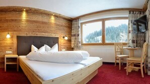 Ein Zimmer aus Holz mit einem Bett, einem Schreibtisch und einem Fenster mit Blick auf Bäume.
