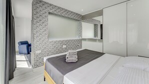 A modern hotel room with a large bed, a blue chair, and a geometric-patterned wall. - Bal One bedroom apartment Adults Only (204) (Arona)