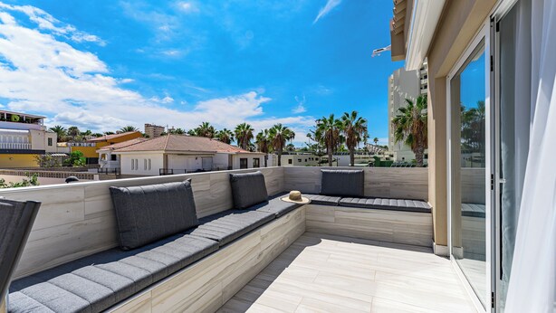 A rooftop terrace with a built-in seating area, a glass door, and a view of palm trees and buildings. - Bal One bedroom apartment Adults Only (204) (Arona)