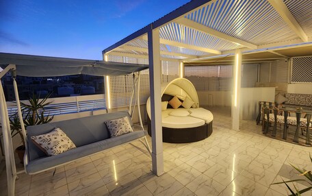 A rooftop terrace with a cushioned seating area, a swing, and a dining set.