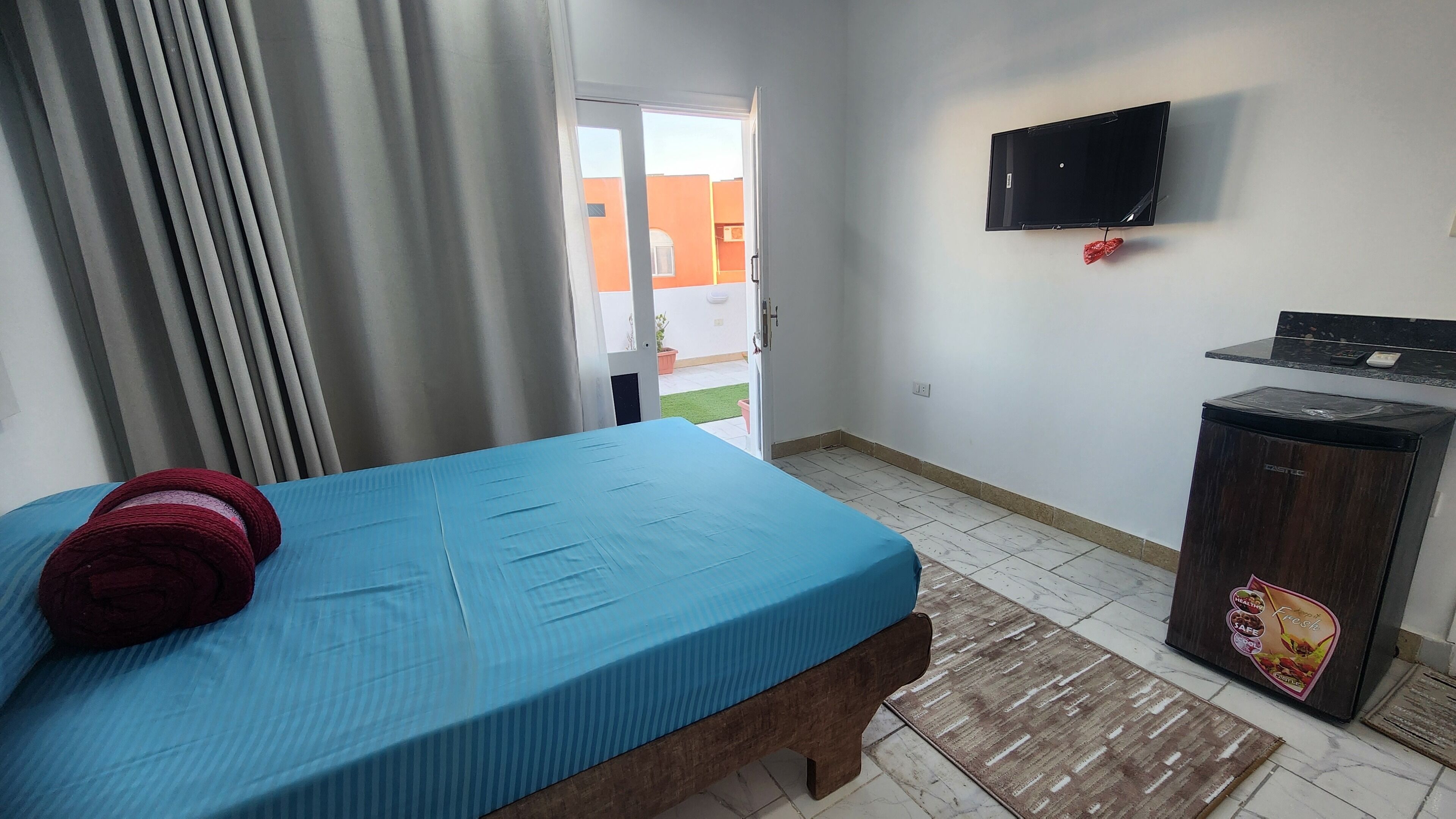 Una stanza con un letto, una TV a parete, una scrivania e un frigorifero.