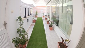 A corridor with a white ceiling, artificial grass, potted plants, and a glass wall on one side. - White Roof - Hurghada (Hurghada)