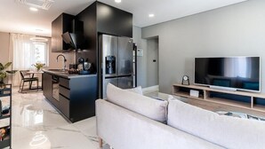 A modern kitchen with a built-in island, a large flat-screen TV, and a minimalist living area with a sofa.