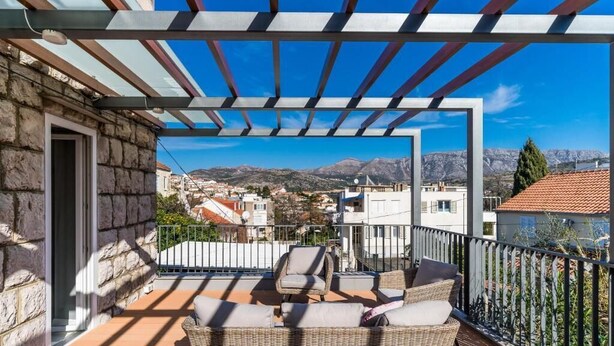 A balcony with wicker furniture and a view of a town and mountains.