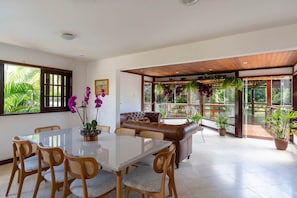 A spacious room with a glass dining table, leather sofa, and potted plants.