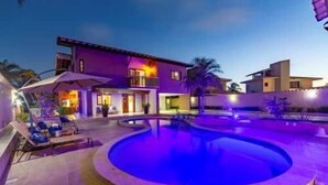 Una piscina con diseño circular, un edificio de varios pisos con balcones y un cielo despejado.
