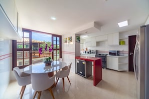 A modern kitchen with white cabinets, a red island, and a dining area with a glass table and chairs.