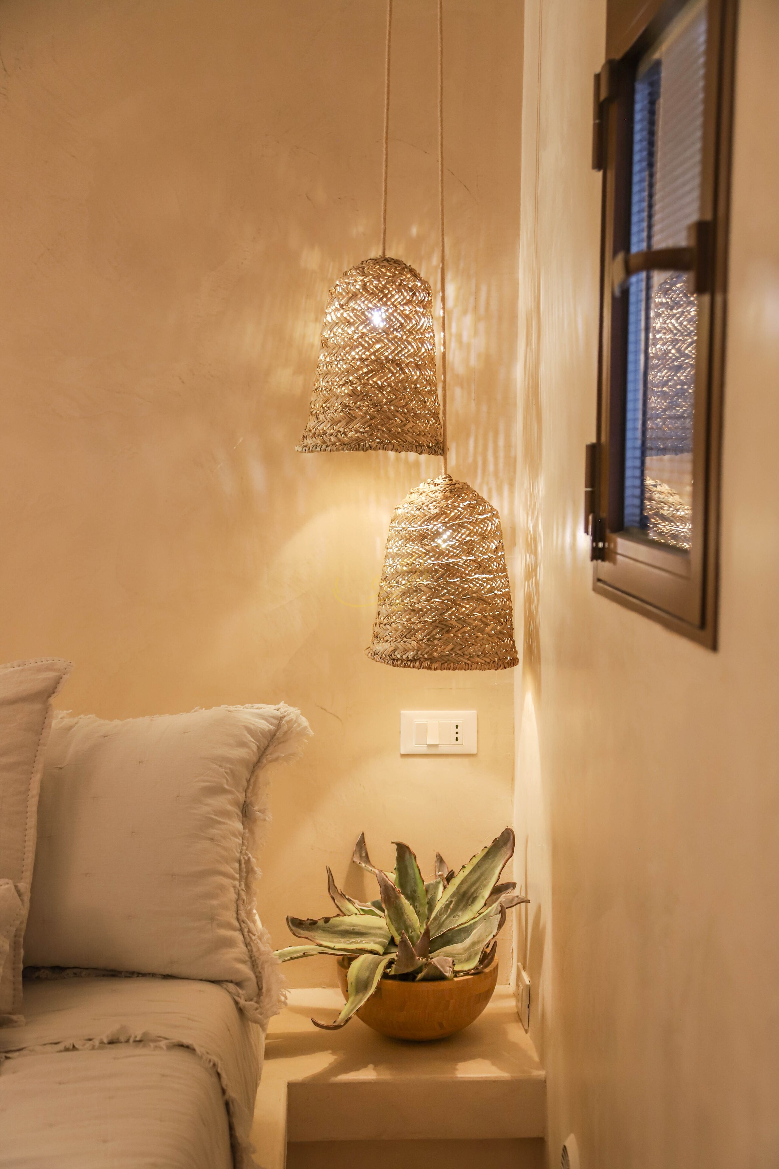 A bedroom with a bed, a bedside plant, and two hanging lamps.