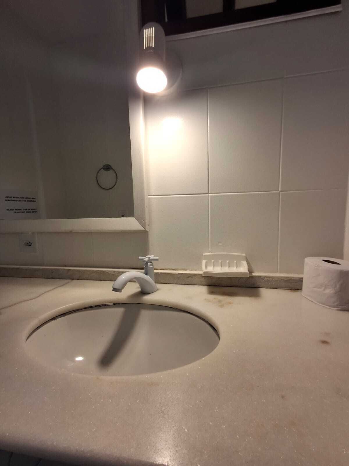 A bathroom with a sink, a toilet paper holder, and a wall-mounted light.