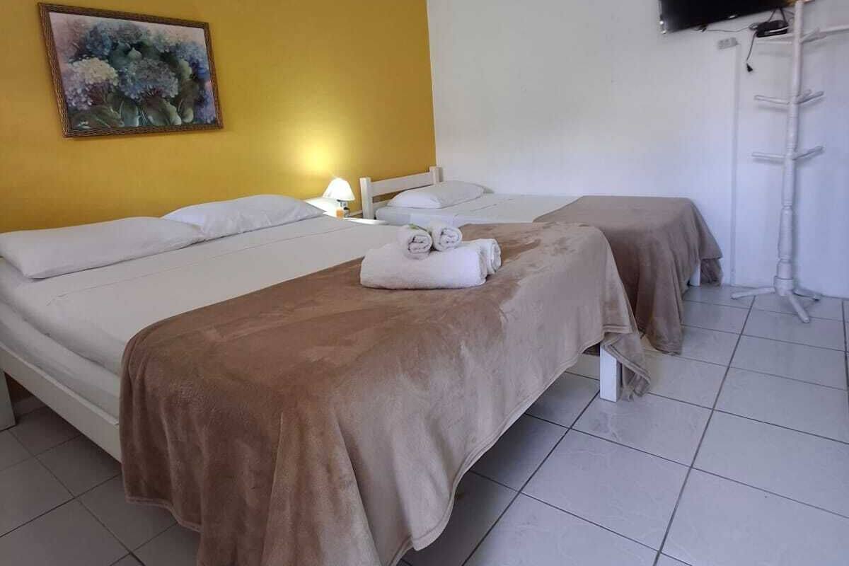 A hotel room with two beds, a ceiling fan, a painting, a TV, and a white floor.
