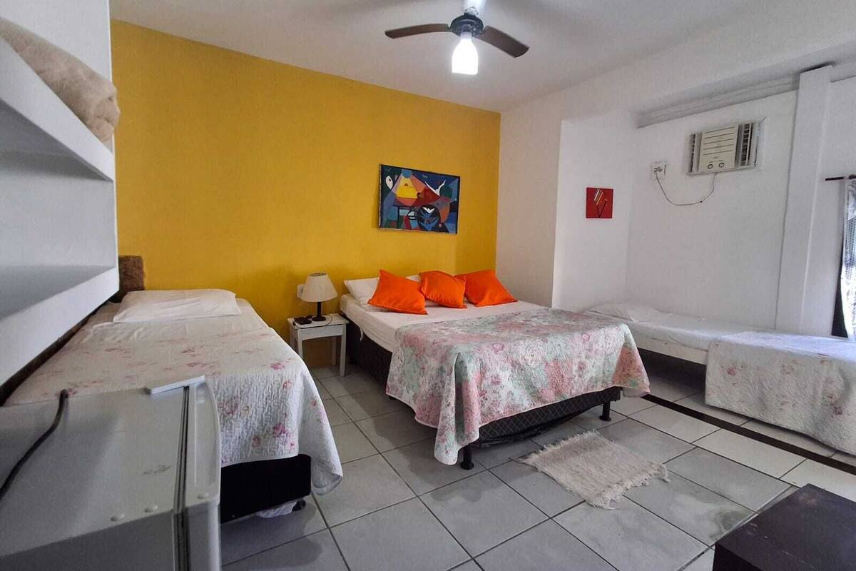 A room with two beds, a ceiling fan, a painting on the wall, and a window with an air conditioning unit.
