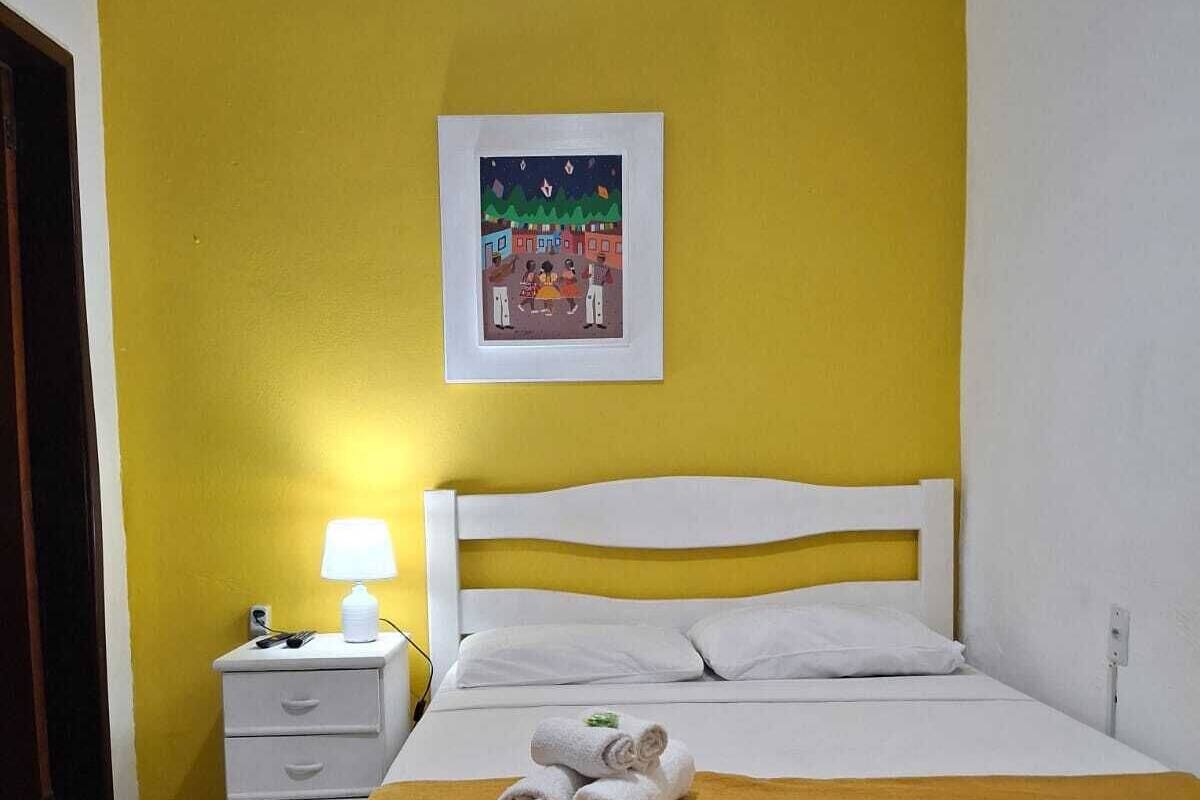A hotel room with a bed, a nightstand, a lamp, and a framed picture on the wall.
