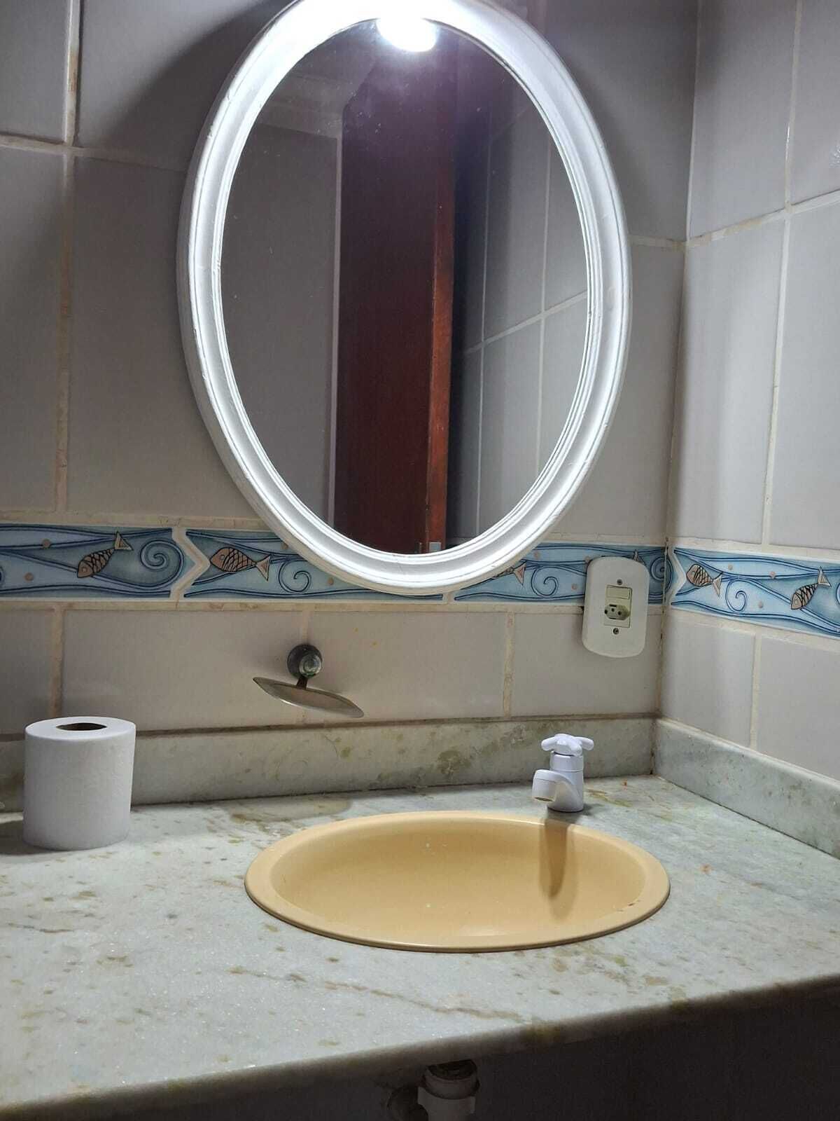 A bathroom with a round mirror, a sink, a toilet paper roll, and a decorative tile backsplash.