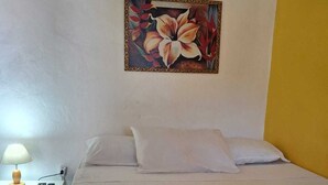 Een hotelkamer met een bed, kussens, een nachtkastje met een lamp en een schilderij aan de muur.