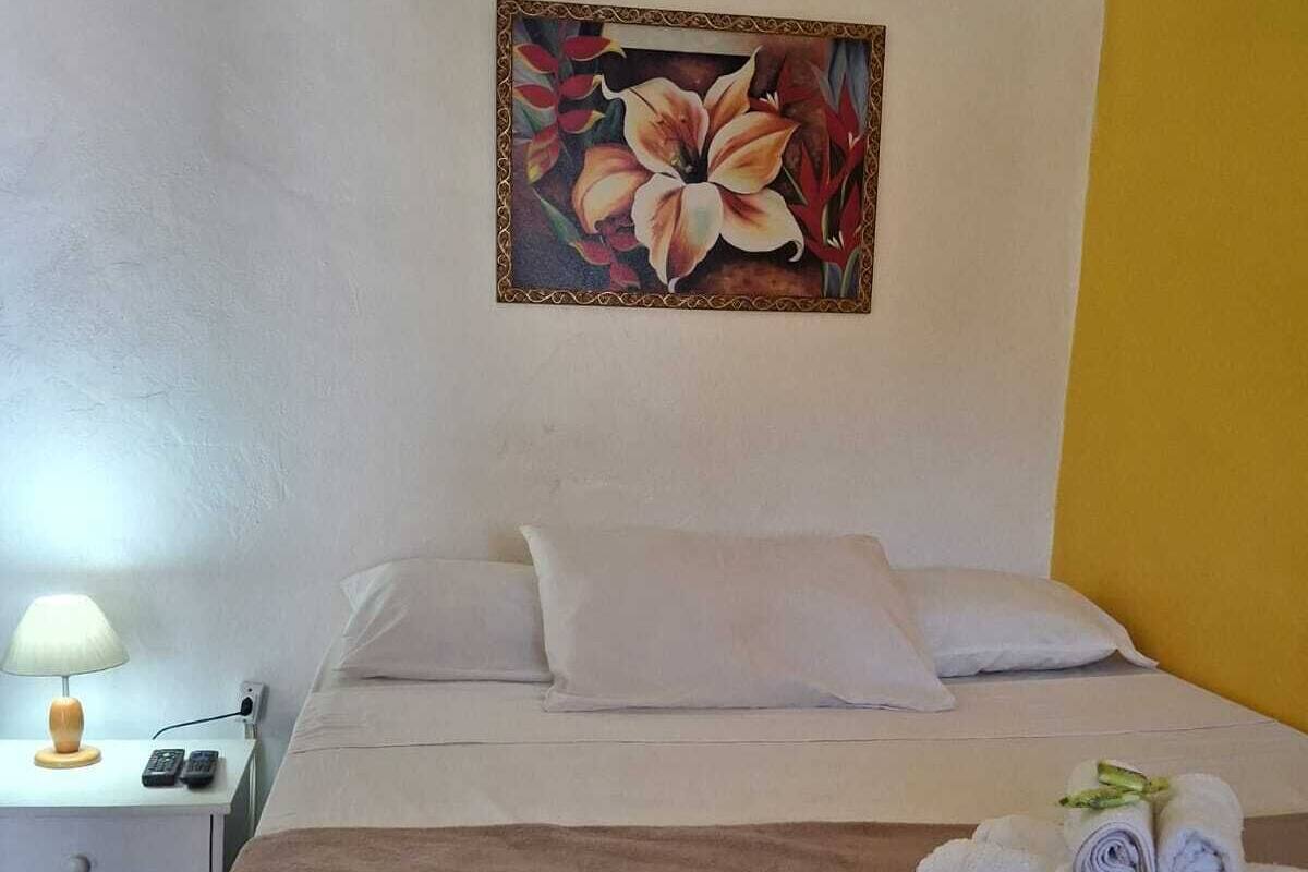 A hotel room with a bed, pillows, a nightstand with a lamp, and a painting on the wall.