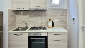 A modern kitchen with light wood cabinets, a stainless steel sink, a gas stove, and an oven.