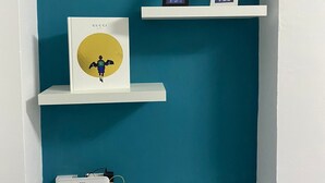 A white shelf unit against a teal wall, holding a framed book, two framed pictures, and a white electronic device.
