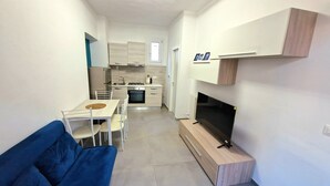 A compact living space with a kitchenette, a dining area with a table and chairs, a sofa, and a TV.