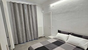 A bedroom with a bed, curtains, a radiator, and a door.