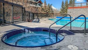 Une piscine avec un jacuzzi, entourée d’une clôture, et offrant une vue sur les montagnes en arrière-plan.