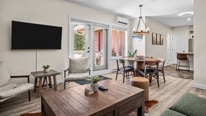 Un salon moderne doté d’un téléviseur à écran plat, d’une table basse en bois et d’un coin repas avec une table ronde et des chaises.