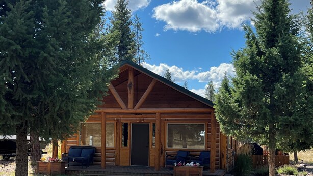 A log cabin with a porch, two blue chairs, and a wooden table. - Charming 2-bedroom cabin with bonus loft, pet-friendly in Seeley Lake (Seeley Lake)