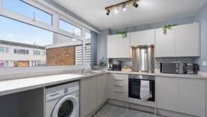 A modern kitchen with a built-in washer, stainless steel appliances, and a view of the neighborhood. - Charming 3 Bedroom House in Birmingham Sleeps 7 (Birmingham)