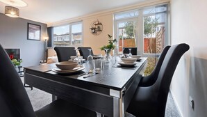 A dining area with a long table set for six, modern chairs, and large windows offering a view of the outside. - Charming 3 Bedroom House in Birmingham Sleeps 7 (Birmingham)