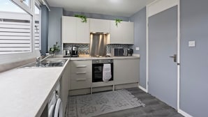 A modern kitchen with a built-in oven, a sink, and a microwave. There is a window providing natural light and a door leading to another room. - Charming 3 Bedroom House in Birmingham Sleeps 7 (Birmingham)