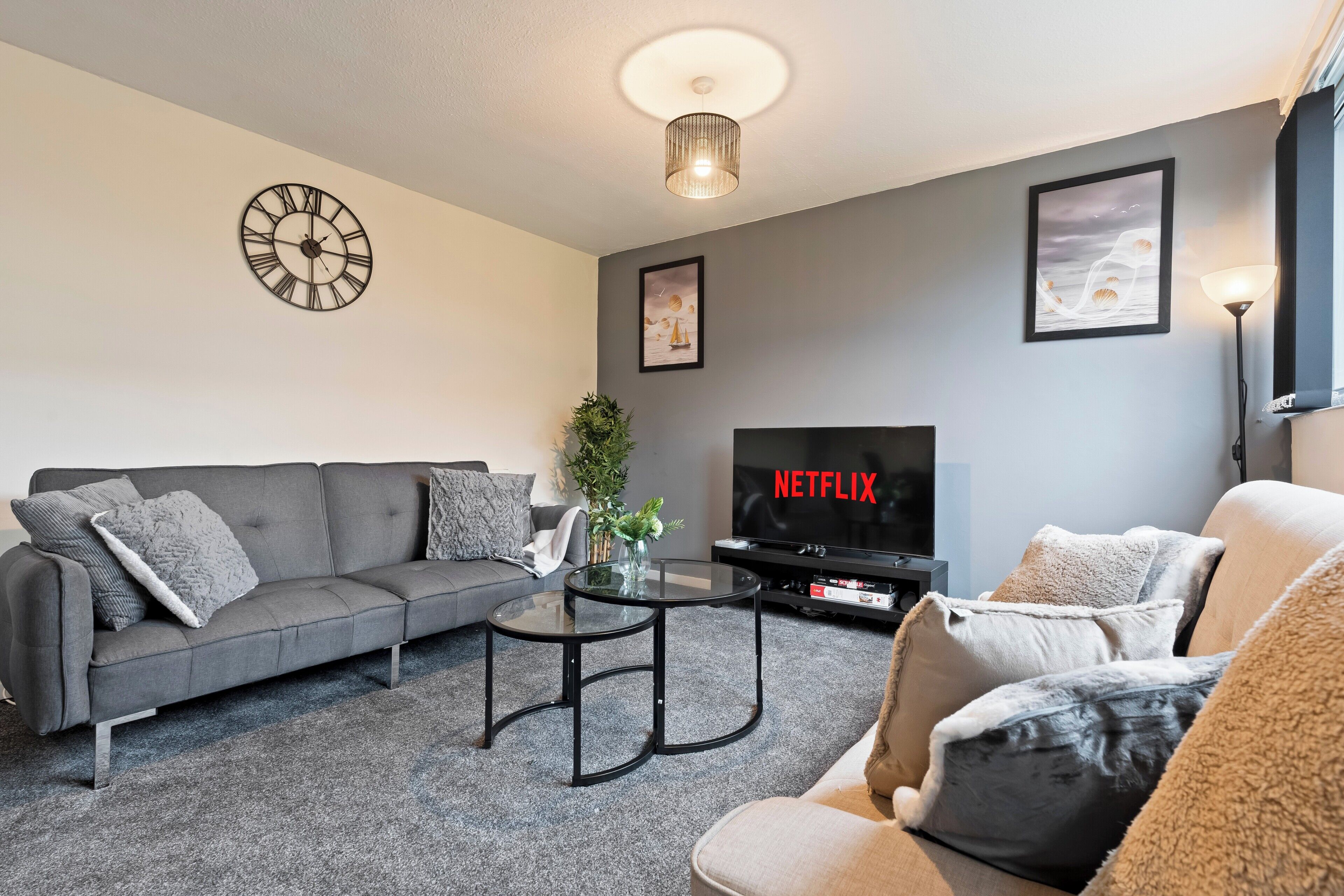 A modern living room with a grey sofa, a round coffee table, and a TV displaying 'NETFLIX'.