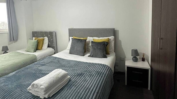 Ein Hotelzimmer mit zwei Betten, einem Schrank, einem Nachttisch mit Lampe und einem Fenster mit Vorhängen.