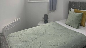 Ein Schlafzimmer mit einem Bett, einem Fenster mit Vorhängen, einem Heizkörper, einer Nachttischlampe und einem Wandbild.